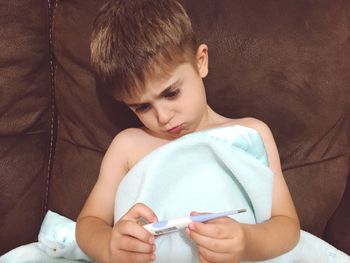 Close-up of boy holding medial equipment while sitting on sofa at home