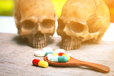 Close-up of wooden spoon with pills and human skulls on table