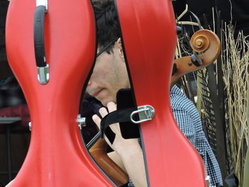 Close-up of man playing cello seen though red case