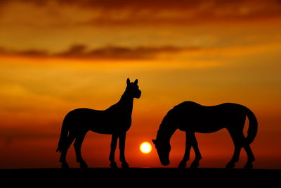 Close-up of silhouette horse toys against orange sky