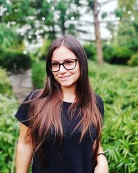 Portrait of smiling young woman standing against plants