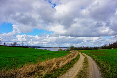 Empty road amidst field against sky