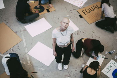 Portrait of bald woman standing while female activists preparing signboards for social issues