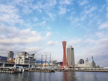 Cranes by river and buildings against sky