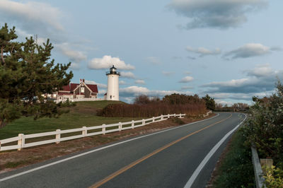 Lighthouse on road against cloudy sky