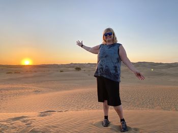 Full length of woman standing on beach against sky during sunset