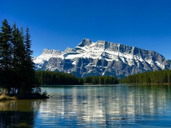 Scenic view of lake by snowcapped mountains against clear blue sky