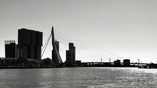 Bridge over river by buildings against clear sky
