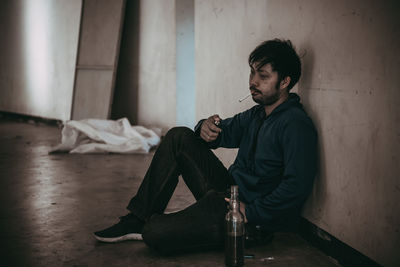 Side view of young man sitting on floor at home