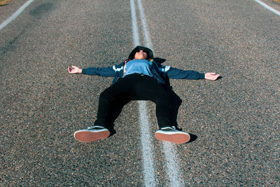 Low section of man lying on the road, tired and arms outstretched