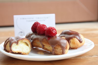 Chocolate eclairs with raspberries in plate on table