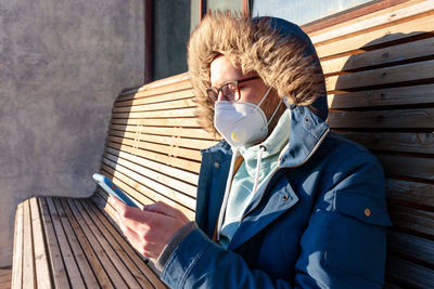 Man wearing mask using smart phone while sitting on bench