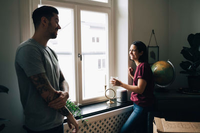 Smiling couple talking while standing by window at new home