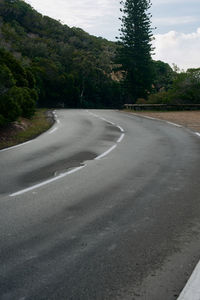 Empty road by trees against sky