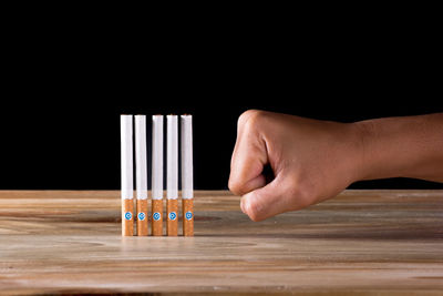 Close-up of hand punching cigarettes on table against black background