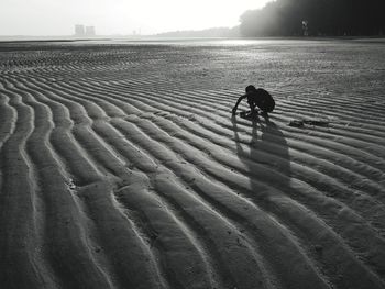 Silhouette man crouching on beach against sky