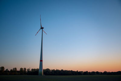 Wind turbines on field against clear sky at sunset
