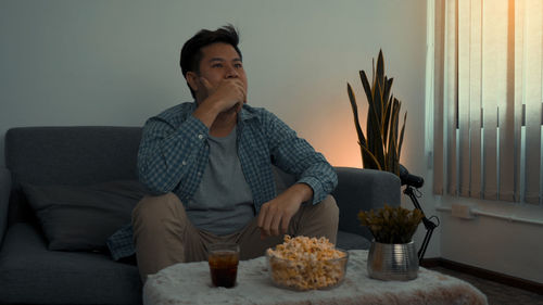 Young man looking away while sitting on sofa at home