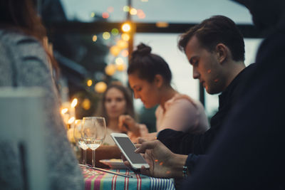 Cropped image of man using smart phone while sitting amidst friends at dining table during dinner party