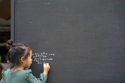 Portrait of cute girl writing alphabet on blackboard