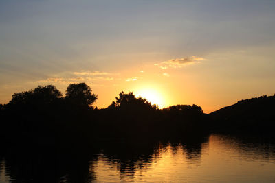 Silhouette trees by lake against sky during sunset