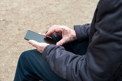 Adult man sits on park bench and uses smartphone. 