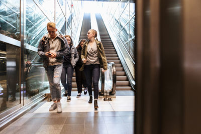 Full length of teenagers walking against escalator
