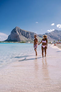 Rear view of women walking on shore against sky