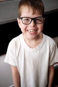 Portrait of a caucsian boy with glasses in a white t-shirt smiling broadly.