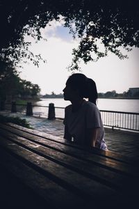 Rear view of woman sitting by lake against sky