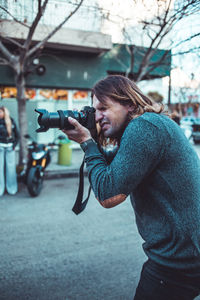 Side view of young man holding camera in city