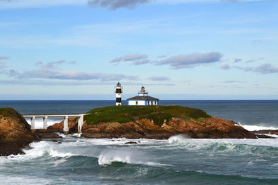 Lighthouse on rock formation in sea against sky