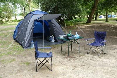 Empty chairs with table and tent at campsite in forest