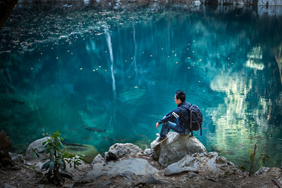 Full length of backpacker sitting on rocks by lake