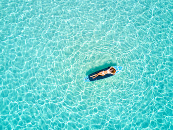 High angle view of woman floating on surfboard over sea