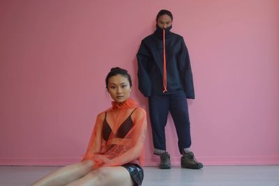 Portrait of young couple sitting against pink wall