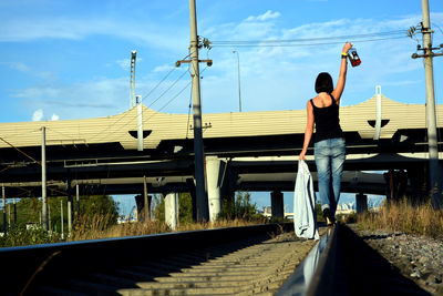 Rear view of drunk woman walking on railroad track while holding liquor bottle
