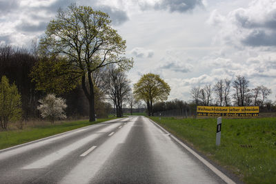 Road by trees on field against sky