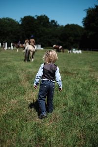 Rear view of boy standing on field against clear sky