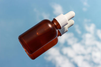 Close-up of hand holding bottle against blue sky