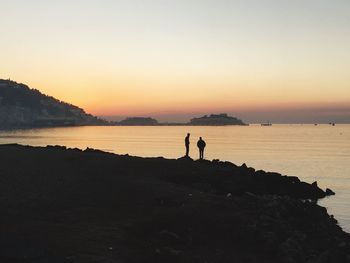 Silhouette people standing at beach against clear sky during sunset