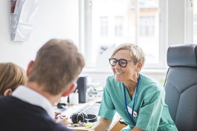 Smiling mature doctor talking to boy with father in clinic