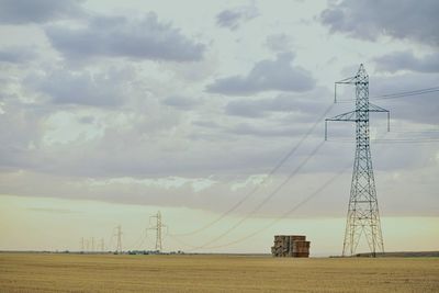 Electricity pylon on field against cloudy sky