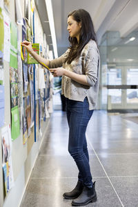 Female university student pinning paper to bulletin board in college
