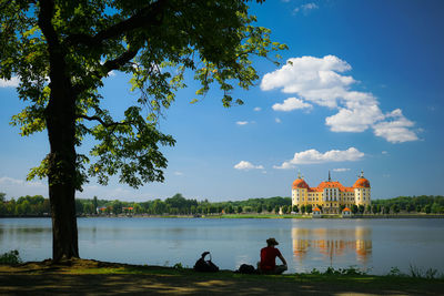 People sitting by lake against sky