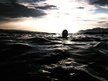 Silhouette man in sea against sky during sunset