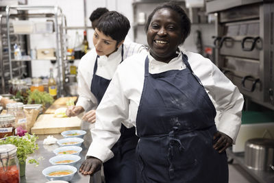 Portrait of smiling chef with female colleague working in background at restaurant kitchen