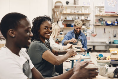 Portrait of smiling woman molding clay sitting by man in art class