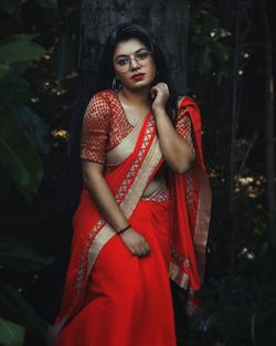 Beautiful young woman standing against trees in saree.