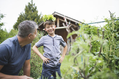 Playful boy with plant on head looking at father in garden